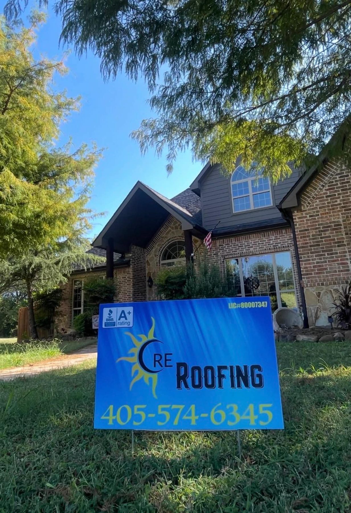 CRE Roofing yard sign showing BBB A+ rating and Oklahoma license number in front of a completed roof