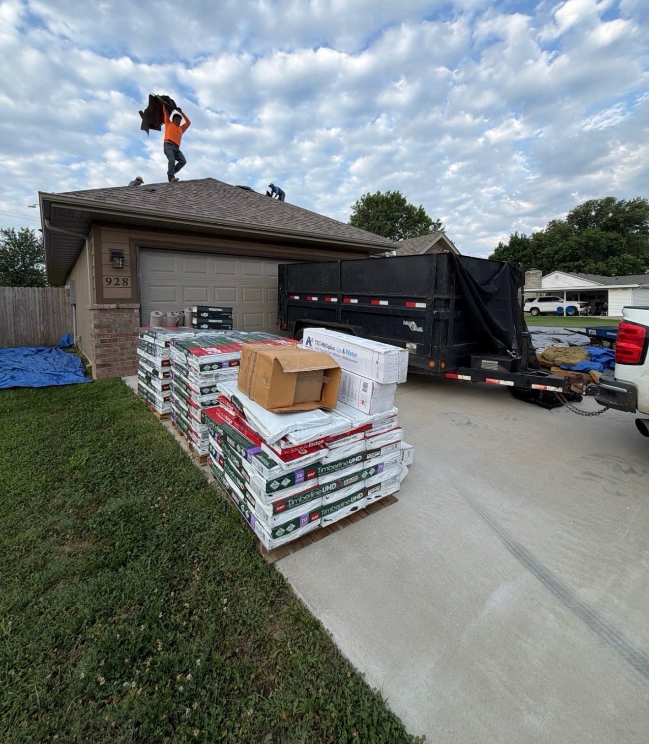 CRE Roofing crew member carrying shingle bundles with pallets staged in the driveway