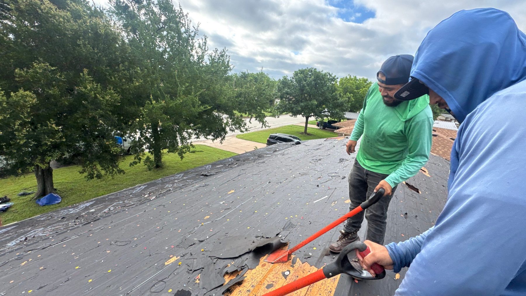 Two CRE Roofing crew members tearing off storm damaged shingles